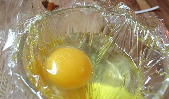 Сырое яйцо в ёмкости с пищевой плёнкой