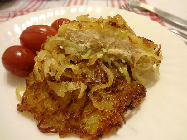 Картофельные драники на тарелке с жареным луком и помидорами