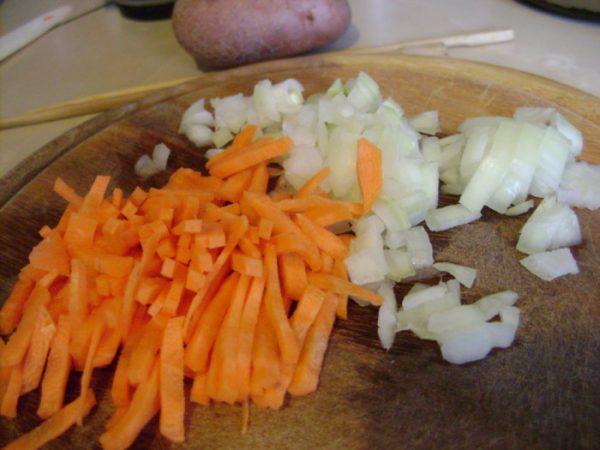Измельчённый репчатый лук и морковная соломка на разделочной доске