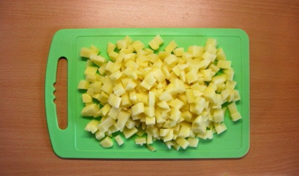 Нарезанный кубиками сырой картофель на разделочной доске
