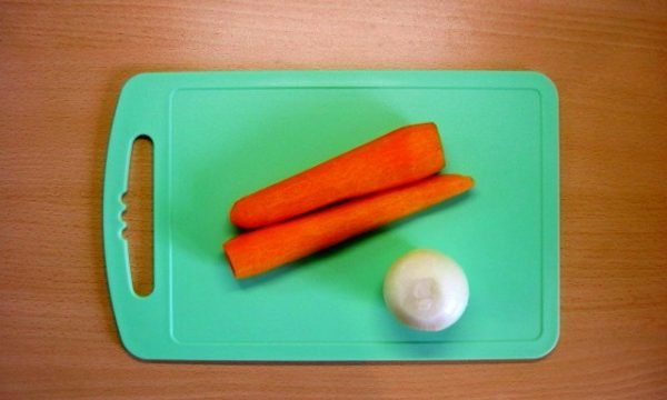 Очищенные лук и морковь на разделочной доске