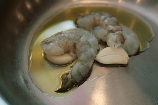 Очищенные креветки и чеснок в сковороде с растительным маслом