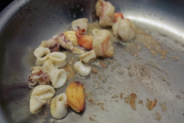 Кальмары, креветки и чеснок в сковородке с растительным маслом