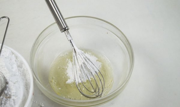 Сахарная пудра в миске со взбитым яичным белком и металлический венчик