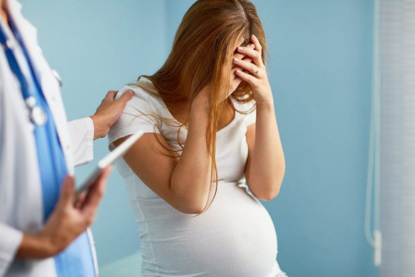 беременная закрывает лицо ладонями, рука врача