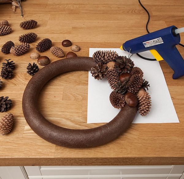 Заготовка для праздничного венка из природных материалов и клеевой пистоле на столе