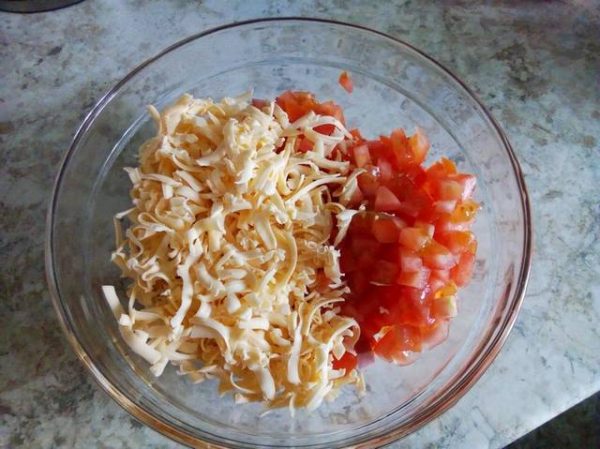 Тёртый твёрдый сыр в стеклянной ёмкости с нарезанными помидорами и колбасой