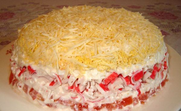 Слоёный салат с крабовыми палочками, помидорами и твёрдым сыром на тарелке