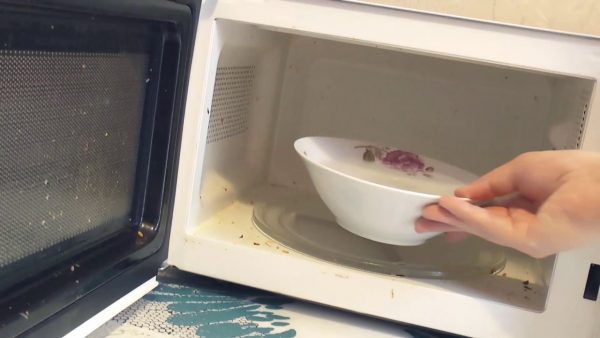 Женщина ставит тарелку с супом в грязную микроволновку