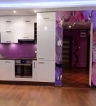 Сочетание фиолетового фартука, белой мебели и ярких обоев на кухне