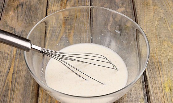 Металлический венчик в стеклянной миске с молоком и сухими дрожжами