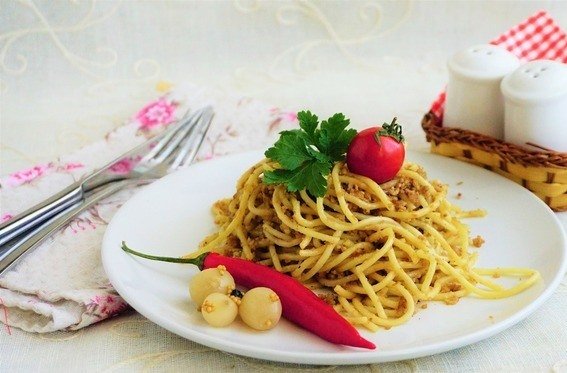 Спагетти с мясным фаршем на белой тарелке, сервированной овощами