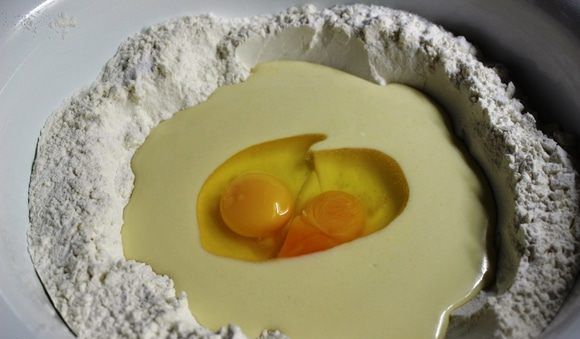 Масляная смесь и сырые яйца в миске с мукой
