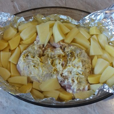 Сырые куриные окорочка и картофель в форме для запекания с фольгой