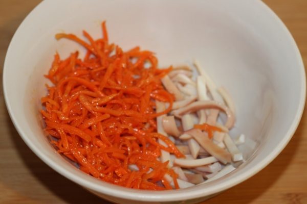 Корейская морковь и нарезанные соломкой отварные кальмары в миске на столе