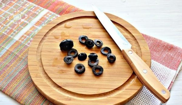 Нарезанные колечками маслина на деревянной разделочной доске с ножом