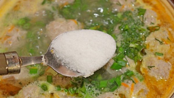 Большая ложка с солью над кастрюлей с супом