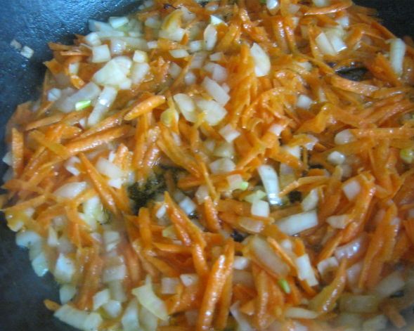 Натёртая на крупной тёрке морковь и рубленый репчатый лук в сковороде