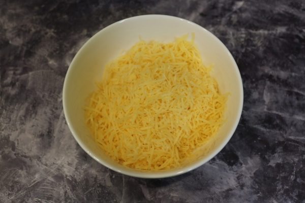 Тёртый твёрдый сыр в белой миске на столе