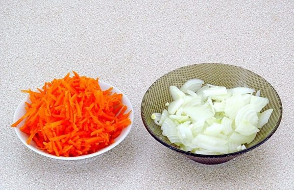 Натёртая на крупной тёрке сырая морковь и нарезанный четвертинками колец репчатый лук в тарелках на столе