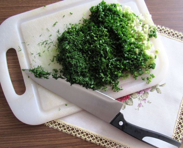 Измельчённая свежая зелень на разделочной доске с большим ножом