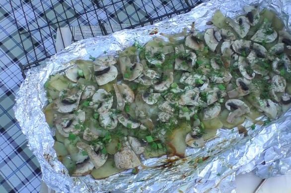Приготовленный на мангале картофель с грибами и луком на листе алюминиевой фольги