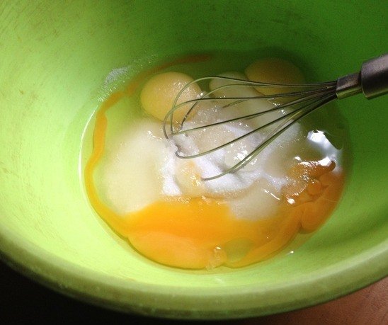Сырые яйца и сахарный песок в зелёной миске с металлическим венчиком