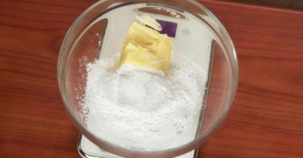 Сахарная пудра и размягчённое сливочное масло в стеклянной миске на столе