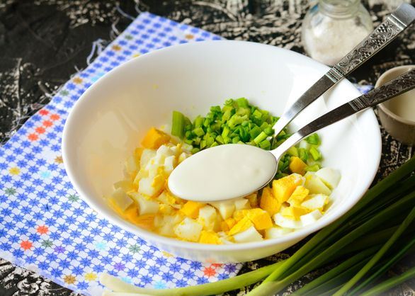 Ложка со сметаной в глубокой тарелке с яично-луковой смесью