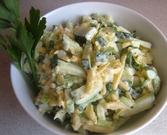 Салат из яиц, зелёного лука, свежих огурцов и сыра в глубокой тарелке на столе