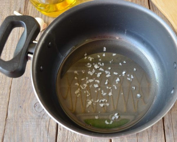Мелко нарезанный чеснок в кастрюле с растительным маслом на деревянном столе