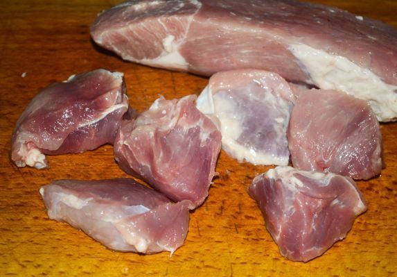 Нарезанное небольшими кусками сырое свиное мясо на деревянной поверхности