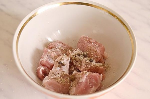 Кусочки сырой свинины со специями в фарфоровой глубокой миске на столе