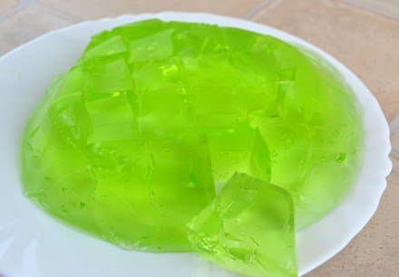 Нарезанное на кусочки зелёное желе на белой тарелке