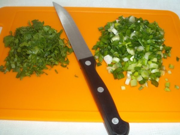 Мелко нарезанная свежая зелень и нож с чёрной ручкой на оранжевой разделочной доске