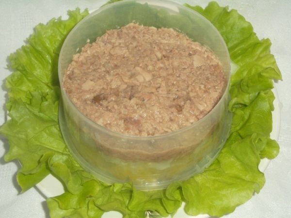 Измельчённая печень трески в пластмассовом формовочном кольце на тарелке с салатными листьями