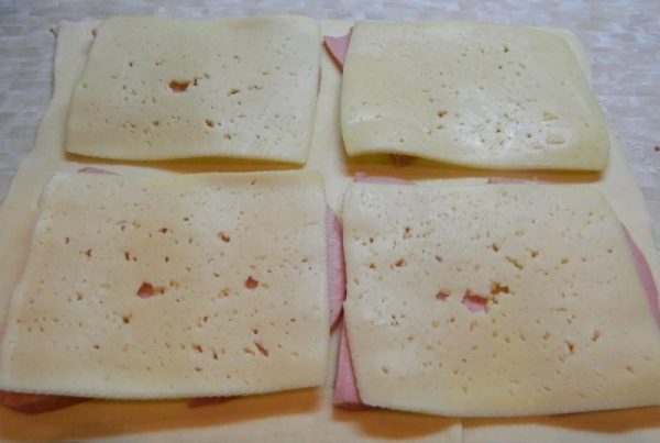 Пласт сырого теста с ломтиками колбасы и твёрдого сыра