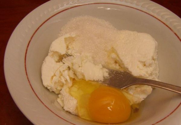 Творог, сахар я сырой яйцо в глубокой тарелке с металлической вилкой