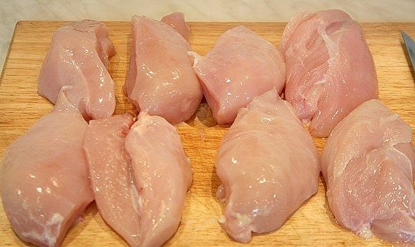 Крупные кусочки сырого куриного филе на деревянной разделочной доске