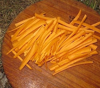 Нарезанная длинной соломкой сырая морковь на круглой разделочной доске из дерева