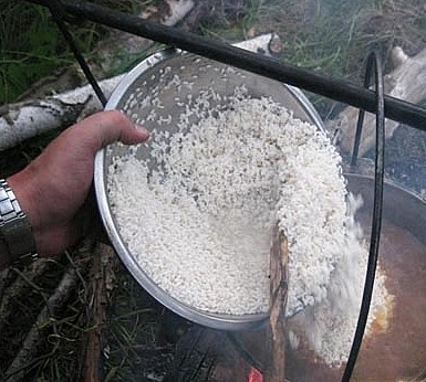 Добавление промытого сырого риса в казан с заготовкой для плова на костре